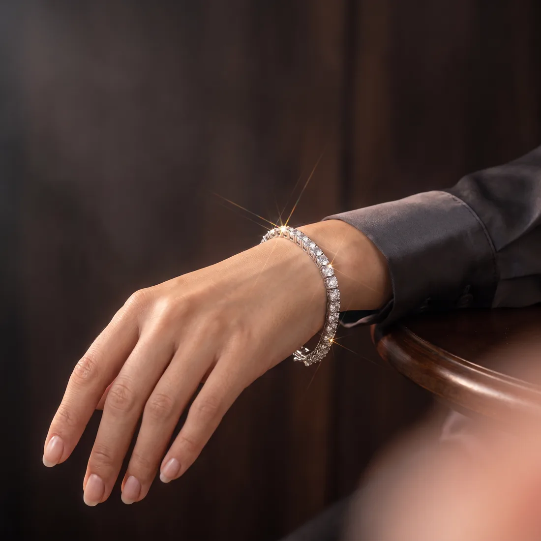 The tennis bracelet worn on a model's wrist against dark walnut